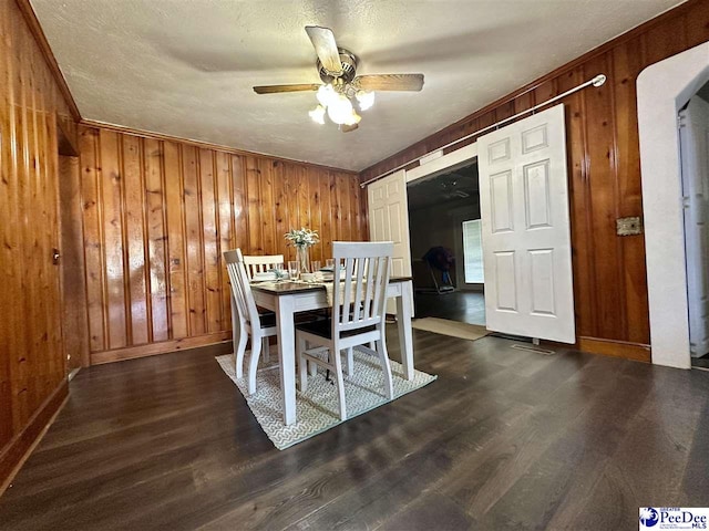 dining room with ceiling fan, dark hardwood / wood-style floors, and wood walls