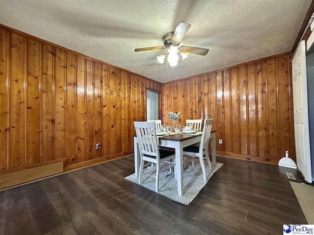 unfurnished dining area featuring ceiling fan, a textured ceiling, dark hardwood / wood-style flooring, and wood walls