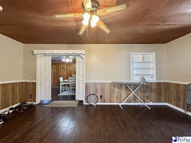 empty room with ceiling fan, wooden walls, dark hardwood / wood-style flooring, and built in shelves