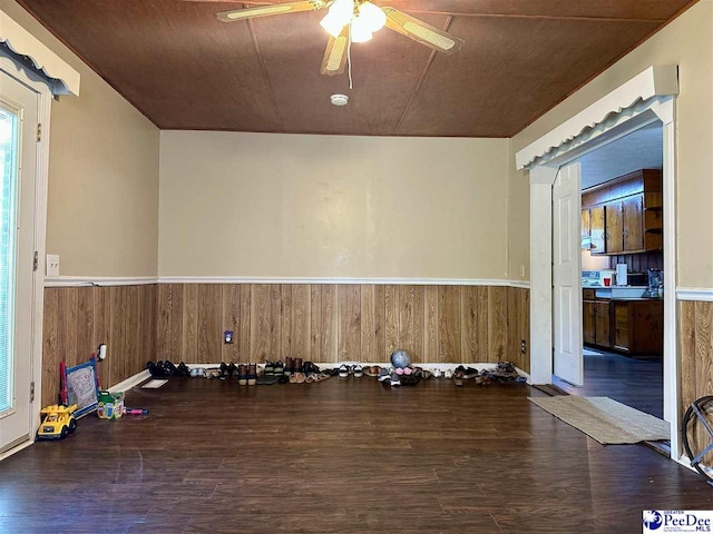 workout room featuring ceiling fan, dark hardwood / wood-style floors, and wood walls