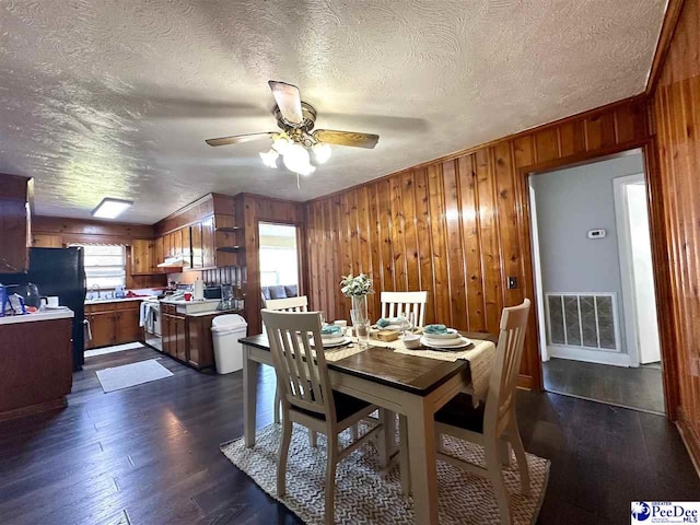 dining room with dark wood-type flooring, a textured ceiling, ceiling fan, and wood walls