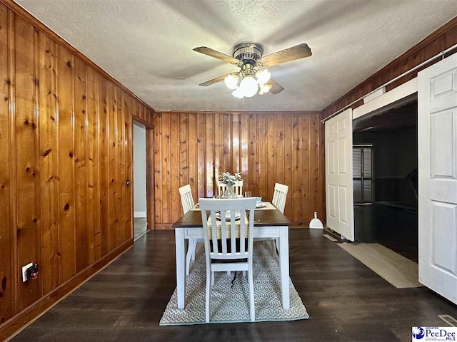 dining area with ceiling fan, dark wood-type flooring, wooden walls, and a textured ceiling