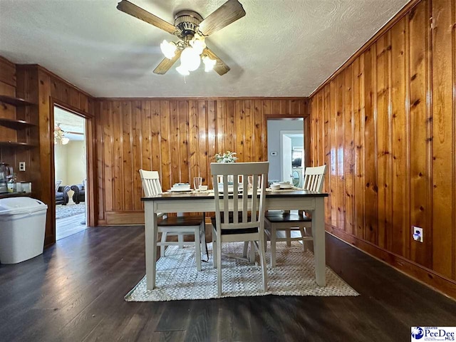 dining room featuring ceiling fan, dark hardwood / wood-style floors, a textured ceiling, and wooden walls