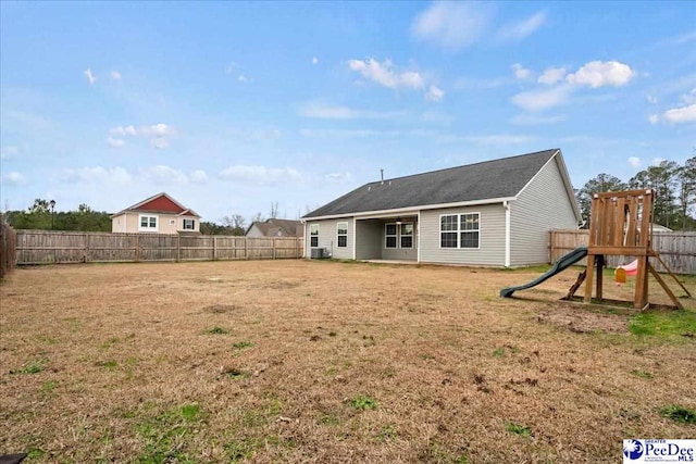 rear view of property featuring central AC unit, a yard, and a playground