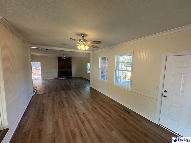 unfurnished living room featuring ornamental molding, plenty of natural light, a large fireplace, and dark wood-type flooring