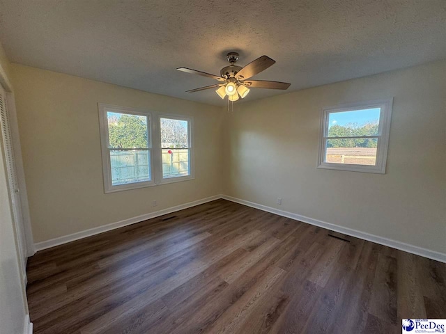 empty room featuring ceiling fan, plenty of natural light, dark wood-type flooring, and a textured ceiling