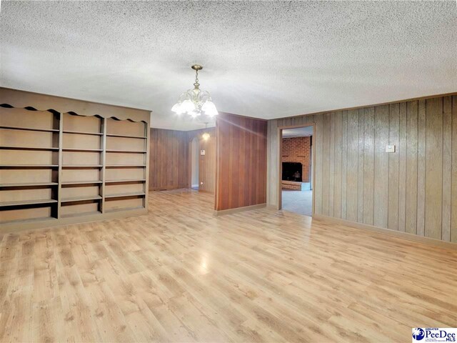 1709 N Irby St, Florence, SC 29501 - empty room featuring wood finished floors, a textured ceiling, a chandelier, wooden walls, and a brick fireplace