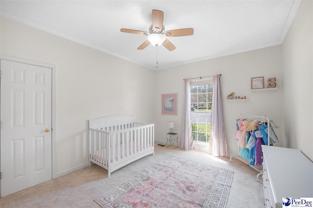 carpeted bedroom featuring a textured ceiling, crown molding, ceiling fan, and a nursery area