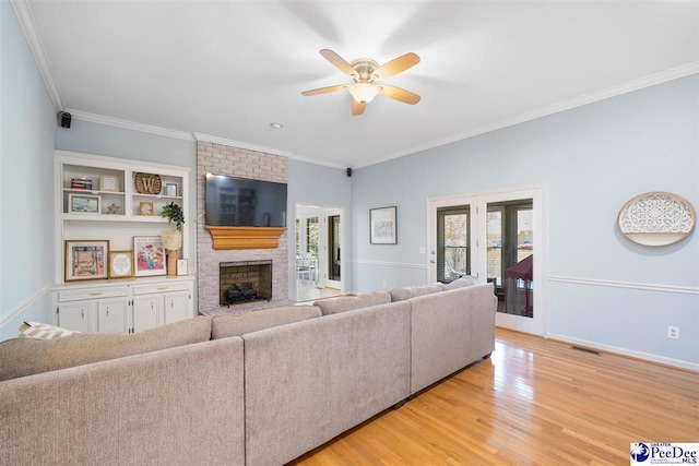 living area with a fireplace, light wood-type flooring, visible vents, ceiling fan, and ornamental molding