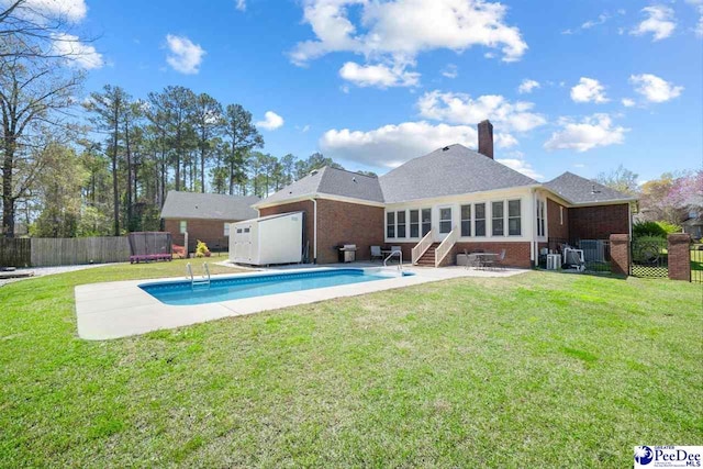 rear view of house with a fenced in pool, fence, brick siding, a patio, and a lawn