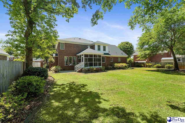rear view of house featuring a fenced backyard, a sunroom, and a lawn