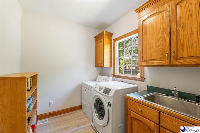 laundry area with light wood-type flooring, washing machine and dryer, a sink, baseboards, and cabinet space