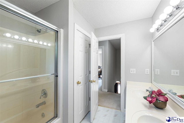 bathroom featuring a textured ceiling, double vanity, a sink, and bath / shower combo with glass door