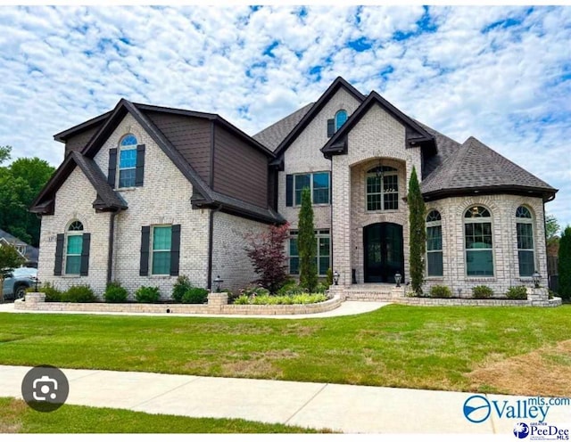 french country inspired facade featuring brick siding, roof with shingles, and a front yard