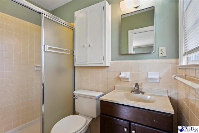 bathroom with vanity, toilet, tile walls, a wainscoted wall, and a shower stall