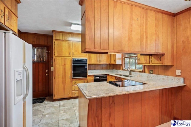 kitchen with brown cabinets, wood walls, a sink, black appliances, and a peninsula