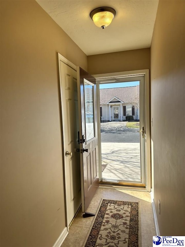 doorway with light tile patterned floors and baseboards