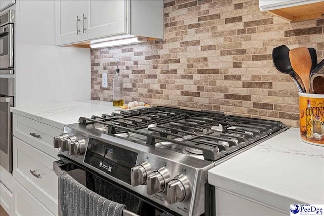 kitchen featuring light stone counters, white cabinetry, stainless steel gas range oven, and decorative backsplash