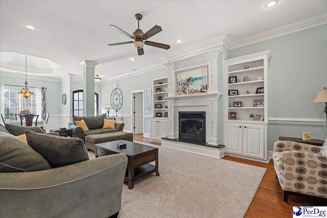 living room with crown molding, hardwood / wood-style flooring, built in features, ceiling fan, and decorative columns