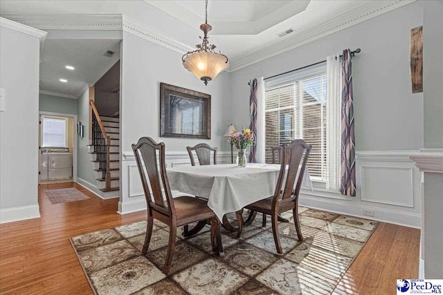 dining area with hardwood / wood-style flooring, ornamental molding, and a raised ceiling