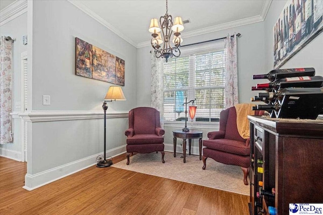 sitting room with crown molding, wood-type flooring, and an inviting chandelier