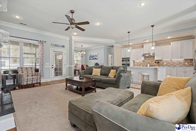 living room with ornamental molding, ceiling fan with notable chandelier, and light wood-type flooring