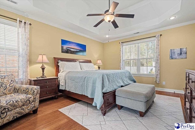 bedroom with crown molding, ceiling fan, a tray ceiling, and light wood-type flooring