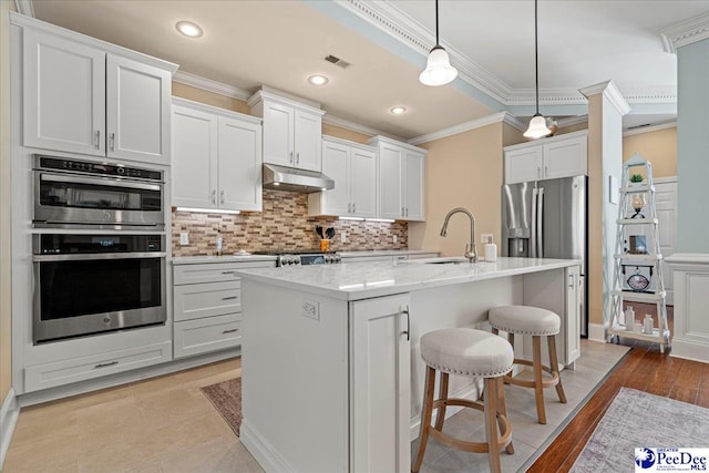 kitchen with hanging light fixtures, appliances with stainless steel finishes, a kitchen breakfast bar, an island with sink, and white cabinets