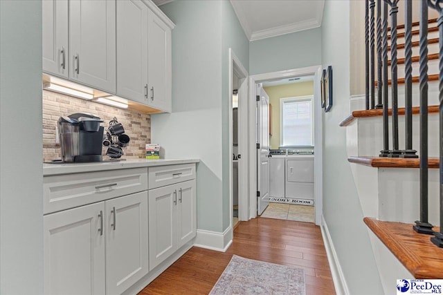 bar featuring washing machine and clothes dryer, white cabinetry, ornamental molding, light hardwood / wood-style floors, and backsplash