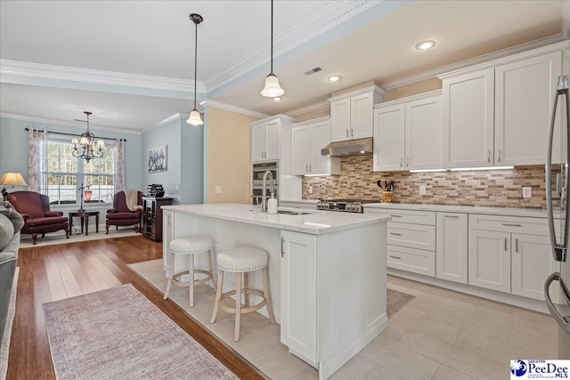 kitchen featuring hanging light fixtures, white cabinetry, sink, and a center island with sink