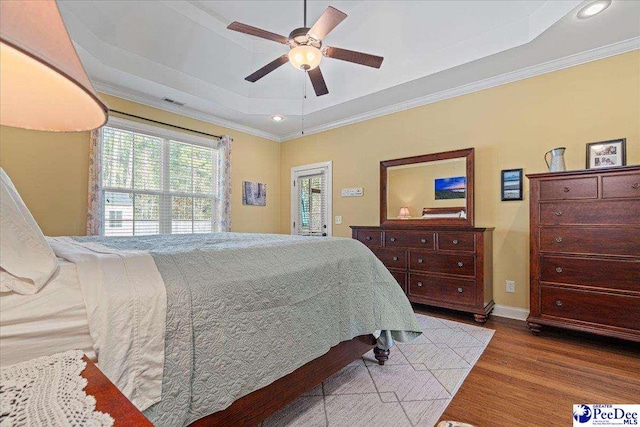 bedroom featuring hardwood / wood-style flooring, ceiling fan, ornamental molding, and a raised ceiling