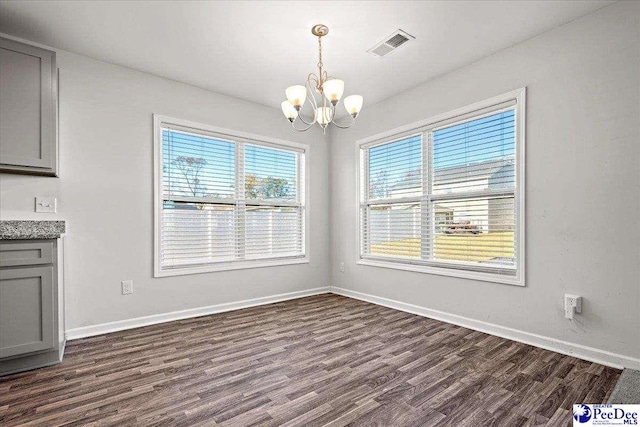 unfurnished dining area featuring dark wood-type flooring, a wealth of natural light, and a notable chandelier