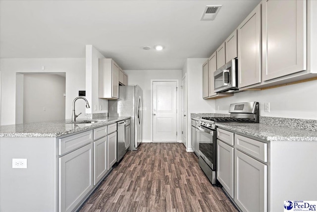 kitchen with sink, gray cabinetry, light stone counters, appliances with stainless steel finishes, and dark hardwood / wood-style floors