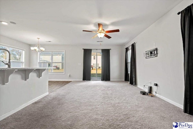 unfurnished living room with sink, ceiling fan with notable chandelier, and carpet