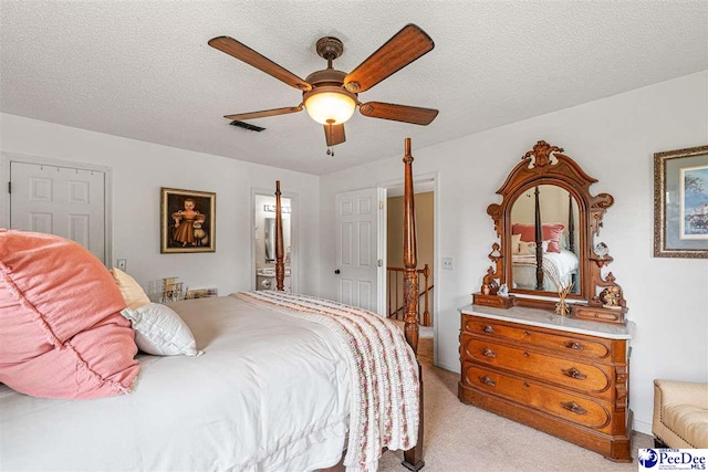 bedroom featuring light colored carpet, a textured ceiling, a ceiling fan, ensuite bathroom, and visible vents