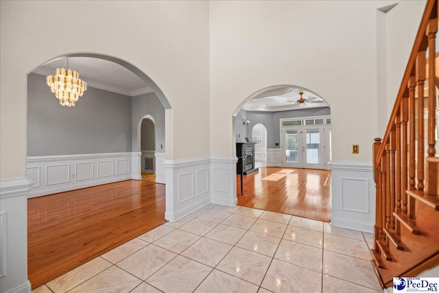 tiled foyer with crown molding, ceiling fan with notable chandelier, and french doors