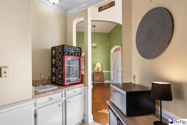 bar featuring sink, hardwood / wood-style flooring, a notable chandelier, ornamental molding, and white cabinets