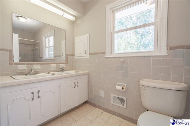 bathroom with tile patterned flooring, tile walls, tiled shower, vanity, and toilet