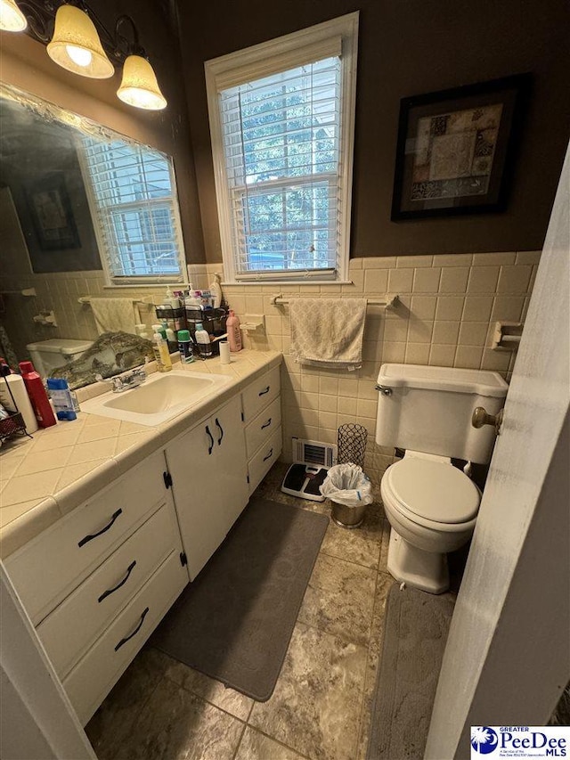 bathroom with vanity, toilet, tile walls, and plenty of natural light