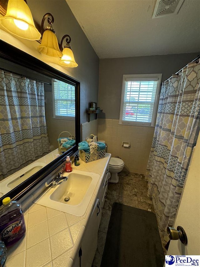 bathroom with tile walls, vanity, toilet, tile patterned floors, and a textured ceiling