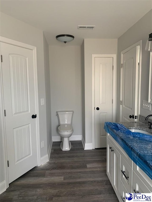 bathroom featuring toilet, wood finished floors, vanity, visible vents, and baseboards