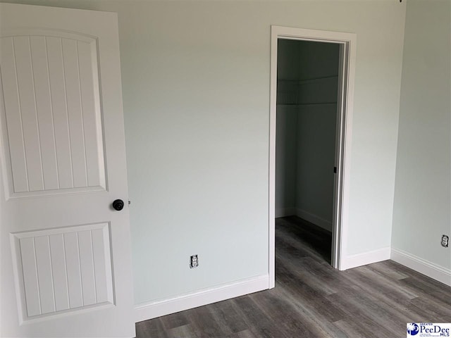 unfurnished bedroom with dark wood-style flooring, a spacious closet, and baseboards