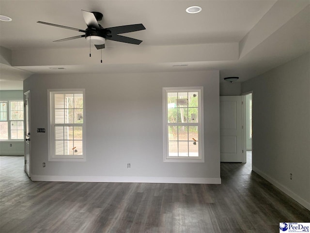 empty room featuring baseboards, dark wood finished floors, a ceiling fan, and a raised ceiling