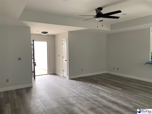 empty room with dark wood-style floors, a raised ceiling, ceiling fan, and baseboards