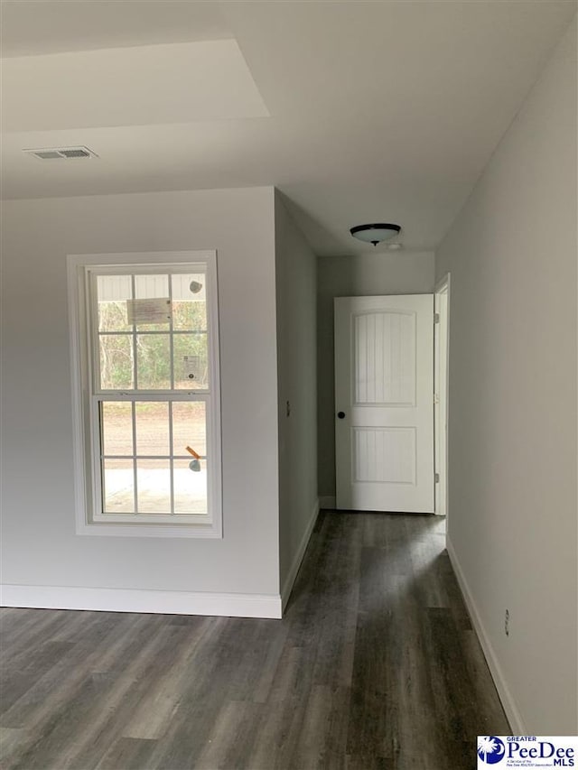 hall featuring dark wood-style flooring, visible vents, and baseboards