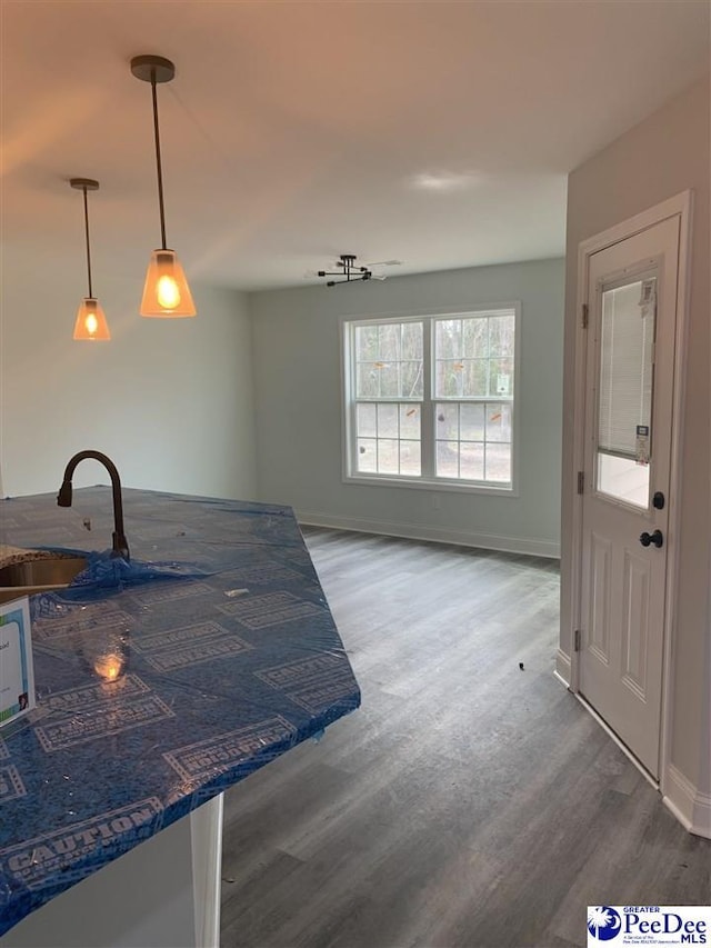 kitchen featuring baseboards, open floor plan, wood finished floors, decorative light fixtures, and a sink