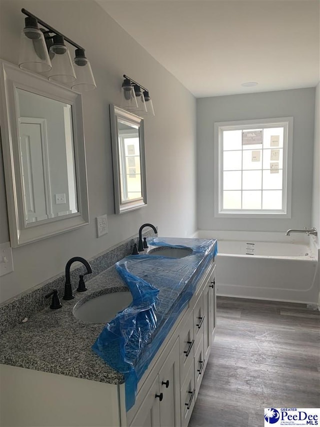 full bath featuring double vanity, a garden tub, a sink, and wood finished floors