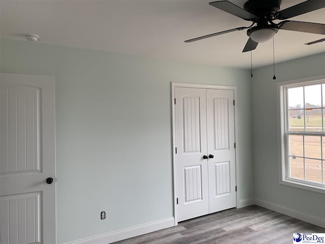 unfurnished bedroom featuring light wood finished floors, multiple windows, a closet, and baseboards