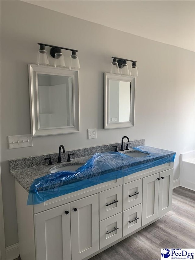 full bath with double vanity, baseboards, a sink, and wood finished floors