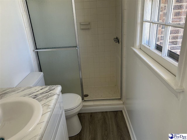 bathroom with baseboards, toilet, a stall shower, wood finished floors, and vanity